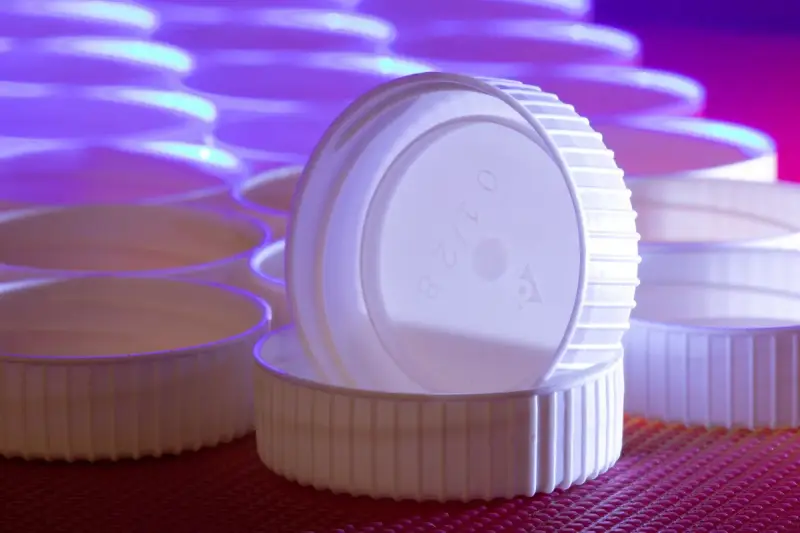 White molded plastic screw caps stacked and standing on edge under violet light