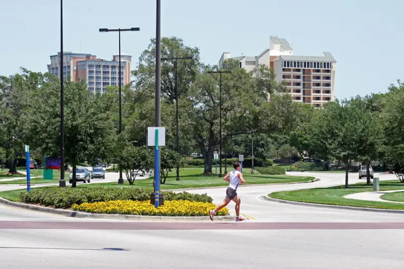 A runner crossing tree-lined Hotel Plaza Boulevard with hotel towers behind in Lake Buena Vista, Florida