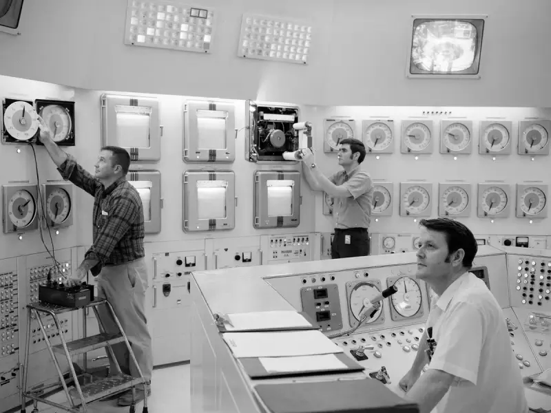 Two operators monitoring a research reactor from a control console