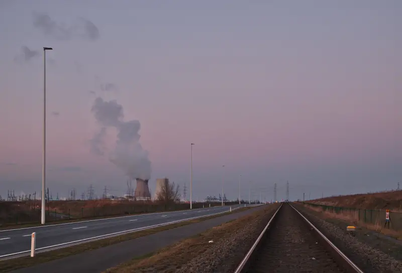 Railway line leading toward a nuclear power station cooling tower at dusk