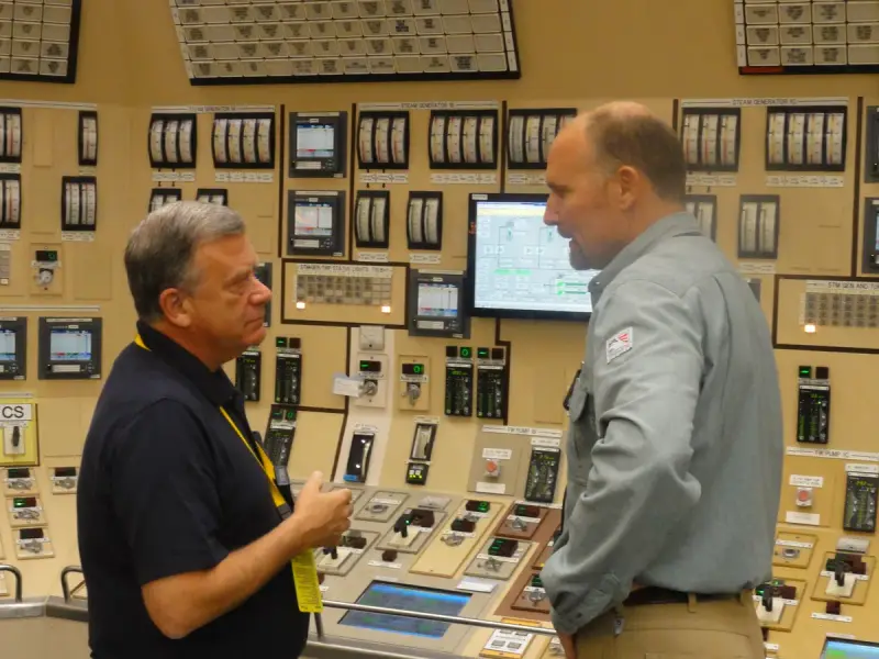 Licensed reactor operator explaining control room panels to a visiting regulator