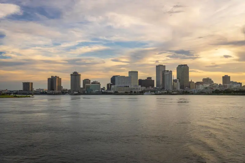 New Orleans skyline seen across the wide Mississippi River under a sunset sky