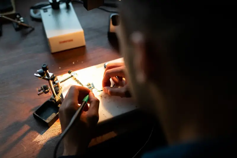Engineer soldering a circuit board under a bright lamp in a workshop