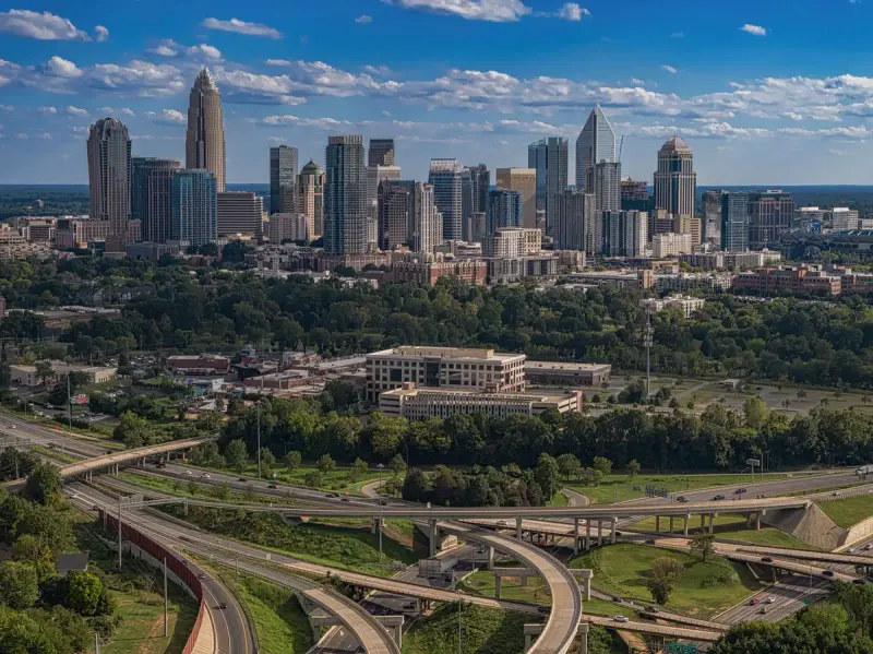 Charlotte skyline above green trees and highway interchanges on a sunny day