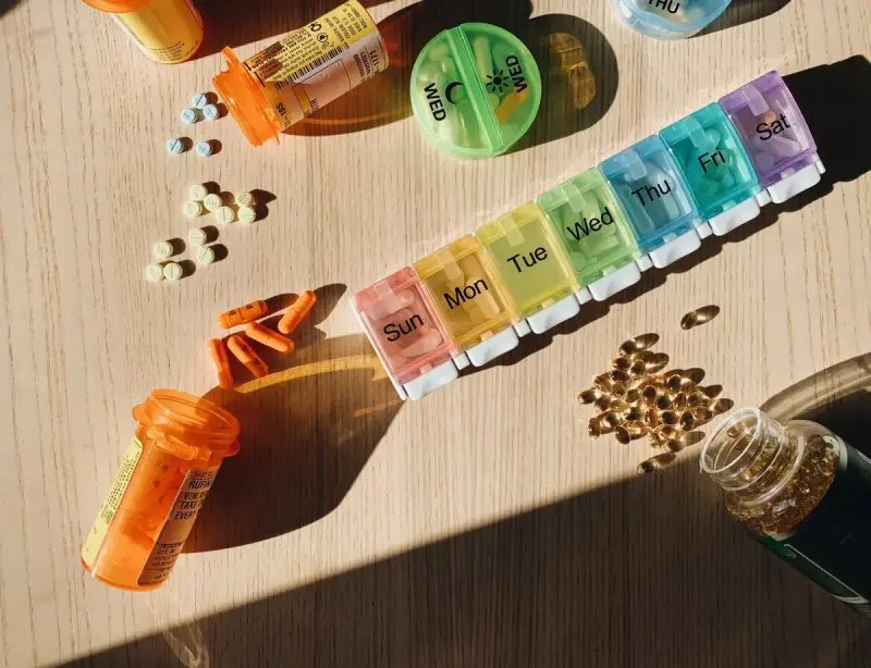 Weekly pill organizer, amber prescription bottles and tablets on a sunlit table