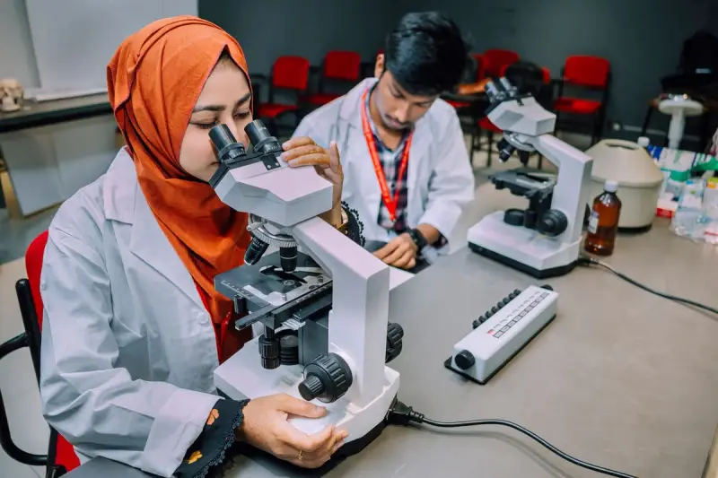 Two students in lab coats working at microscopes in a university teaching lab