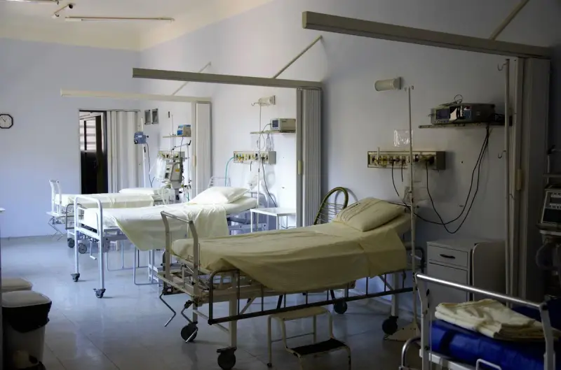 Clean hospital ward with made beds, privacy curtain rails and wall-mounted medical equipment