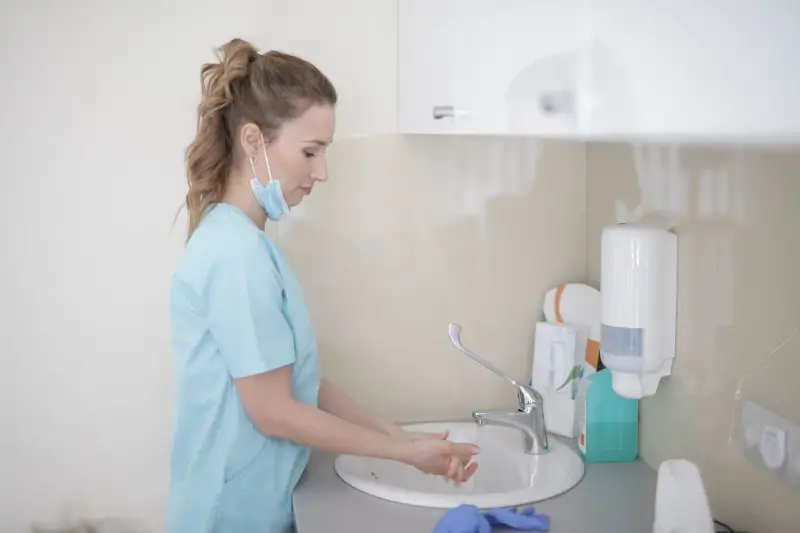 Nurse in scrubs washing her hands at a clinic sink next to a soap dispenser