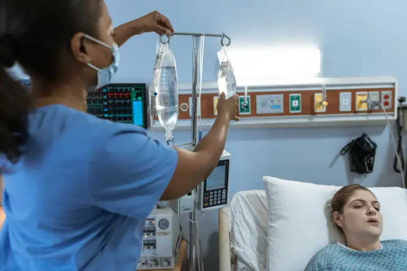 Nurse adjusting an IV drip for a patient resting in a hospital bed