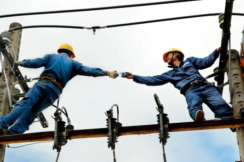 Two electrical workers collaborating on overhead power lines