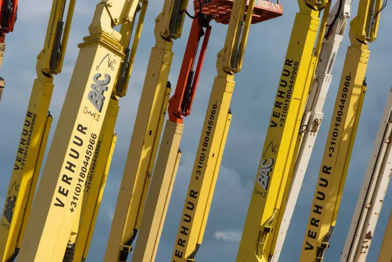 Row of yellow boom lifts extended against a clear blue sky