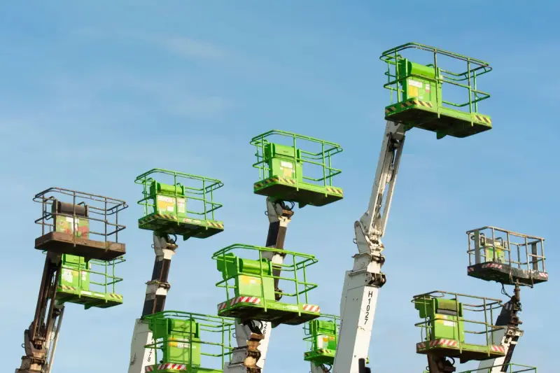 Green cherry picker baskets extended high against a blue sky