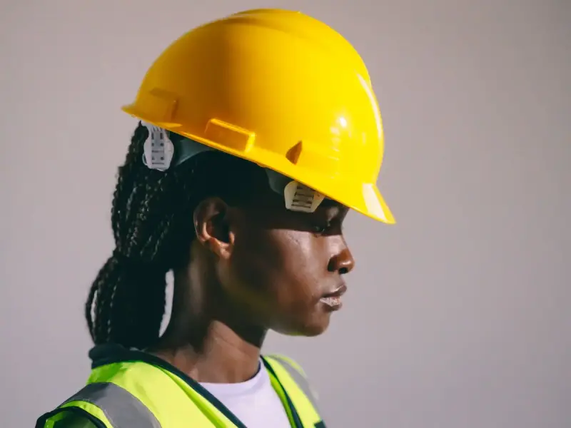 Woman in a yellow hard hat and reflective vest seen from the side