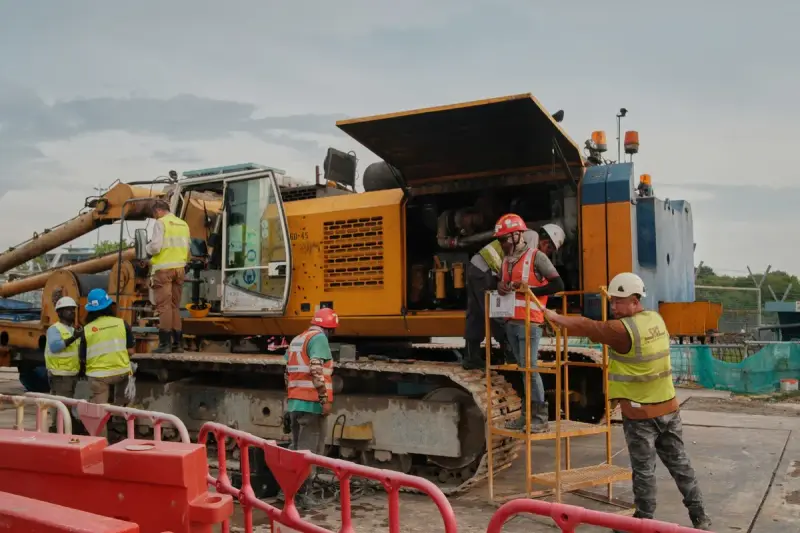 Crew in hard hats and hi-vis vests servicing a tracked drilling rig with its engine cover open