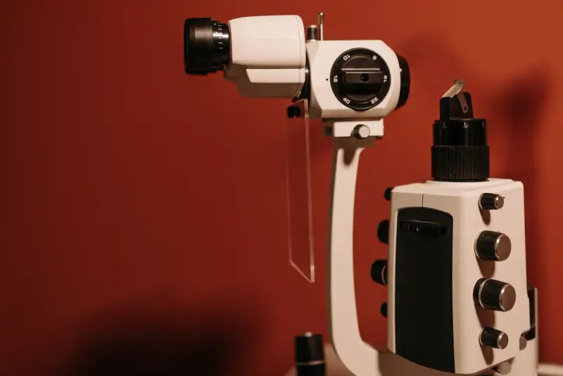White ophthalmic slit lamp microscope against a deep red wall