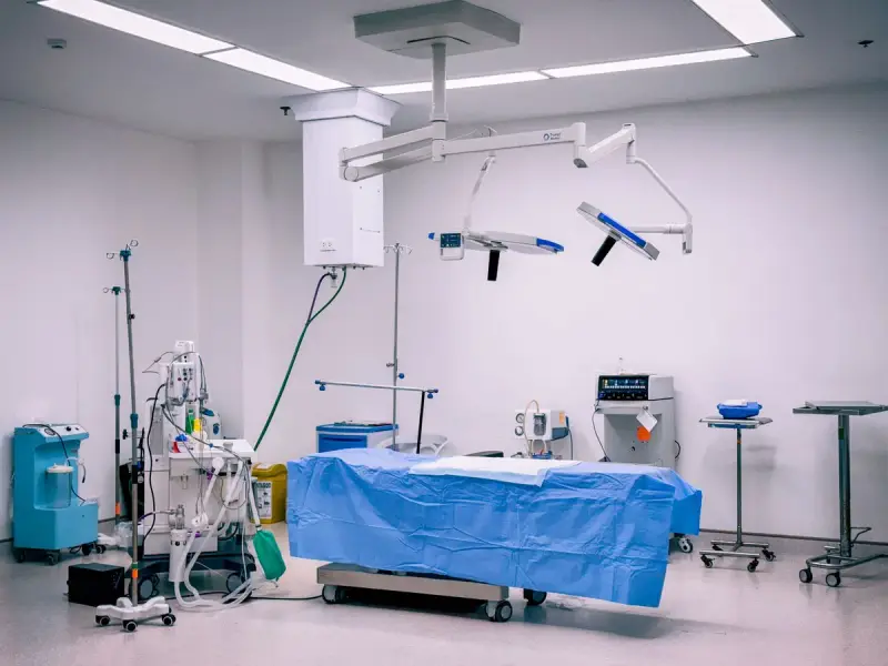Empty operating room with an anesthesia workstation, ceiling-mounted lights and a draped table
