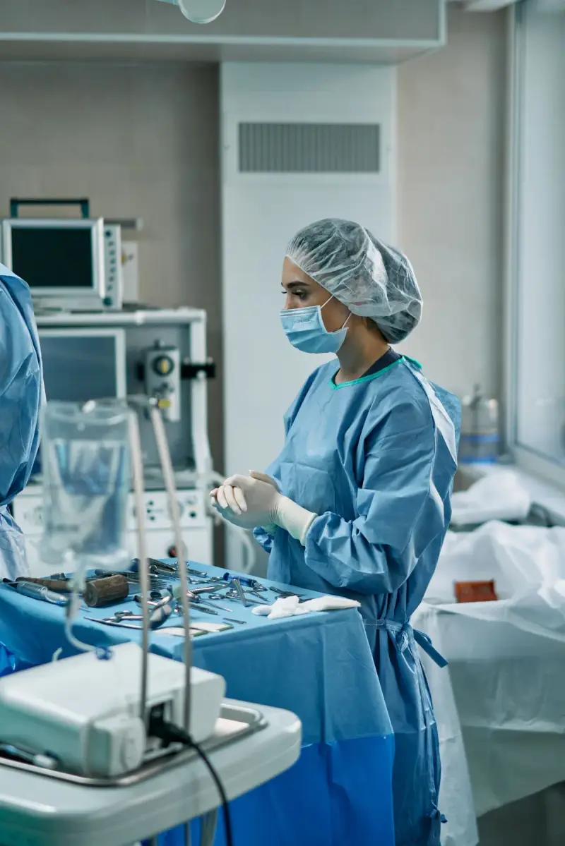 Gowned and masked clinician standing beside an instrument table and monitoring equipment