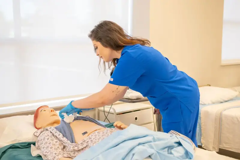 Clinician in blue scrubs practicing on a patient simulation manikin in a training room