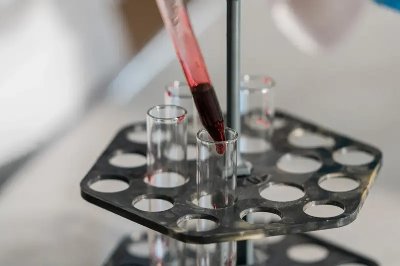 Glass test tubes in a black rack with red liquid being added to one tube