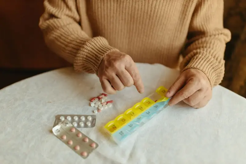 Older hands sorting tablets into a yellow and blue weekly pill organizer