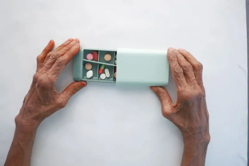 Older hands holding a turquoise pill box with compartments of colorful tablets