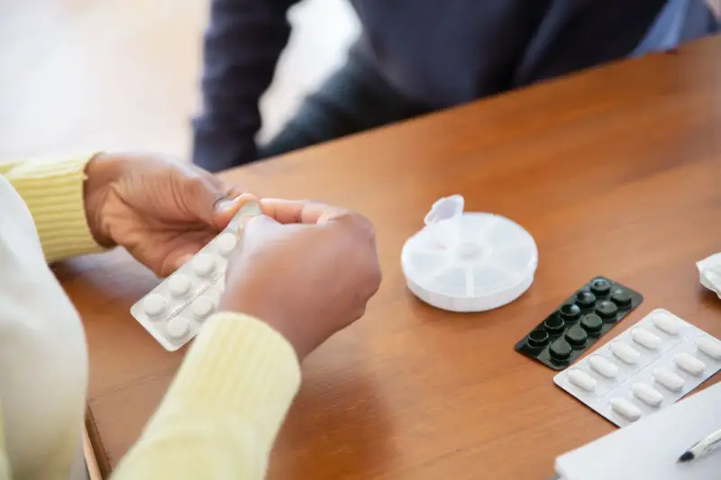 Caregiver in a yellow top pressing tablets from a blister pack beside a pill box