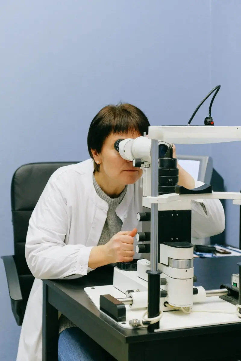 Eye doctor in a white coat looking through a slit lamp microscope at a desk