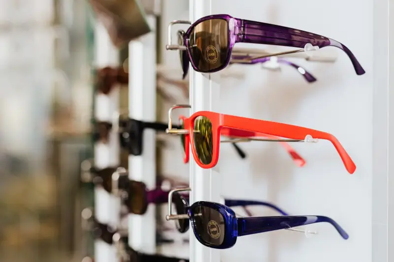 Purple, orange and navy sunglasses hanging on a white wall display