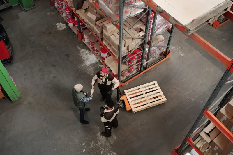 High view of three people talking beside a pallet in a warehouse aisle