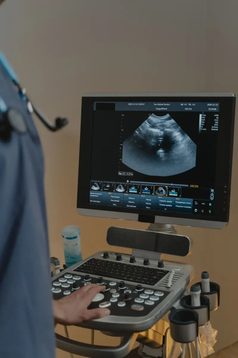 Clinician in blue scrubs with a stethoscope adjusts settings on a cart-based ultrasound system