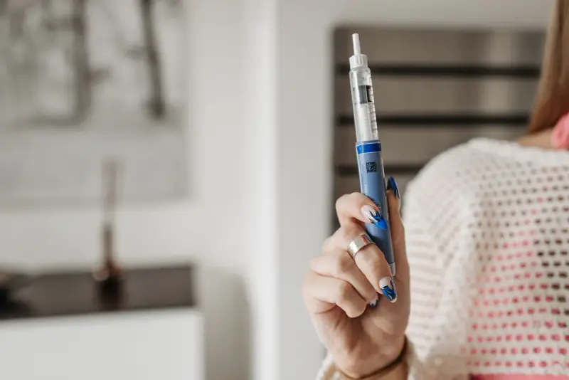 Woman holding up a blue self-injection pen at home