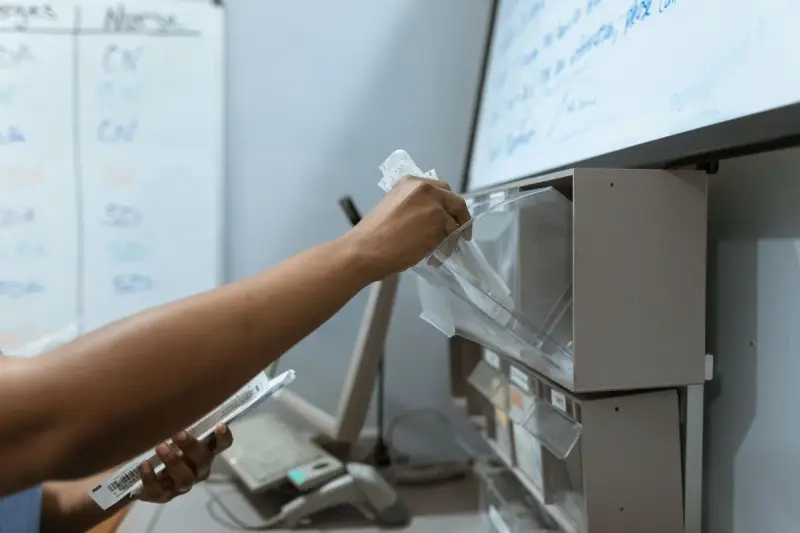 Hand pulling supplies from a clear bin while holding a barcoded package in a clinic