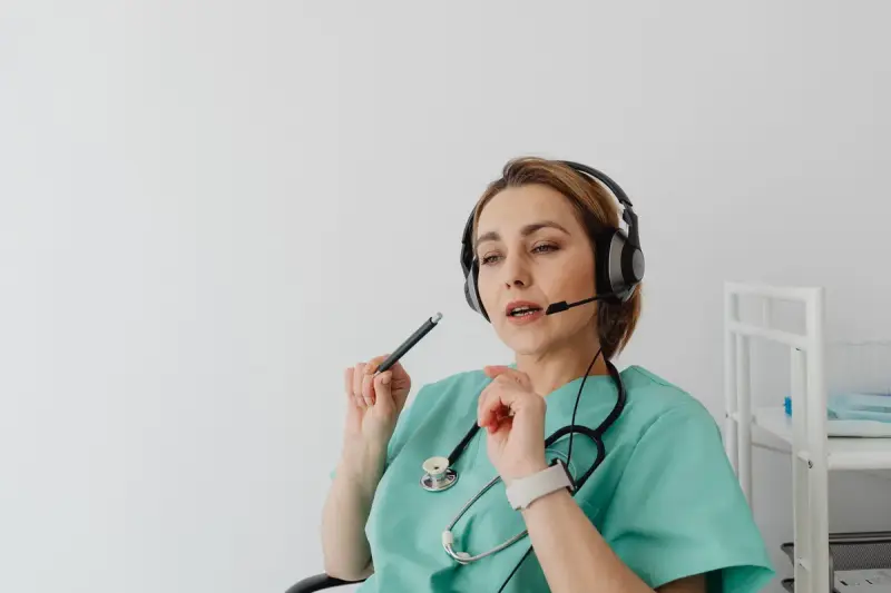 Nurse in teal scrubs and a headset talking with a patient over the phone