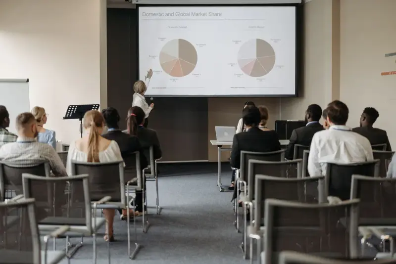 Audience seated in a conference room watching a presenter beside a market share chart