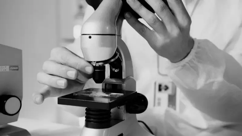 Scientist in a white lab coat looking through a microscope