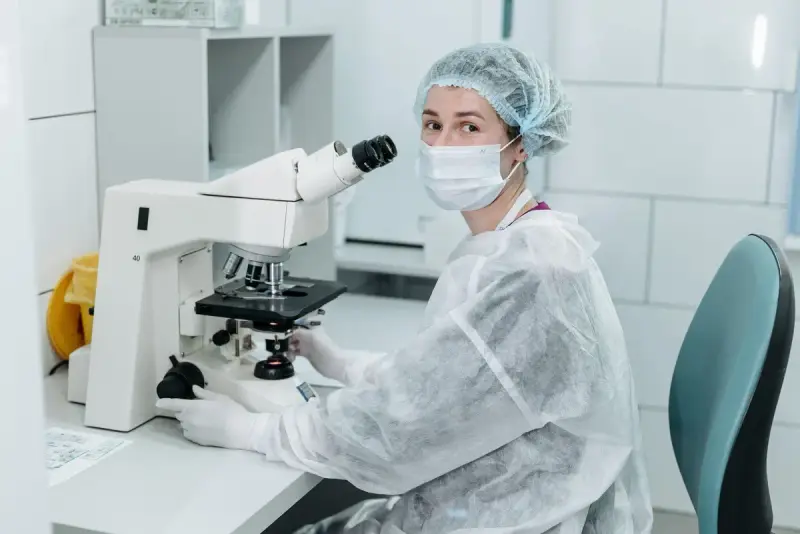 Scientist in protective gear using a microscope in a sterile lab