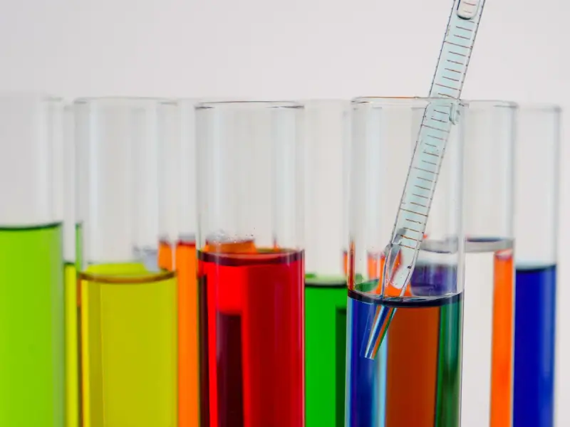 Row of test tubes with green, yellow, red and blue liquids and a pipette in one tube