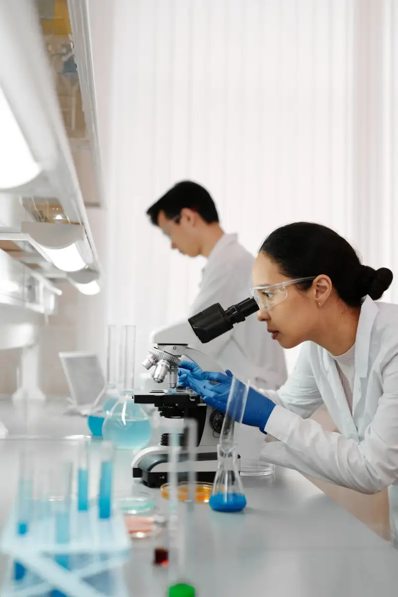 Researcher in a lab coat and safety glasses looking into a microscope