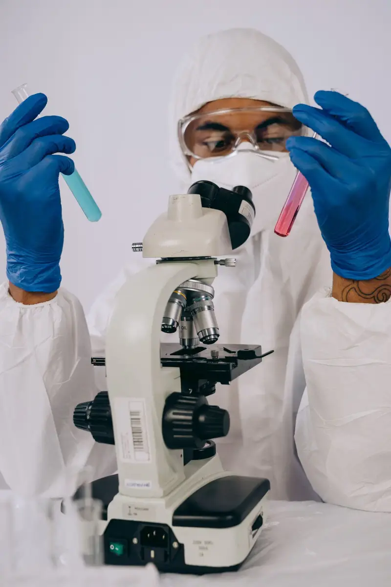 Scientist in protective gear examining a row of test tubes