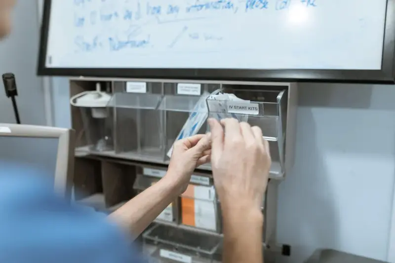 Hands pulling an IV start kit from a labeled supply bin on a hospital unit wall