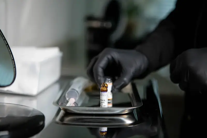 Gloved hand placing a small medicine vial on a stainless steel tray