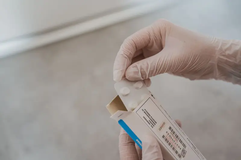 Gloved hands opening a white medication carton and lifting out a blister pack
