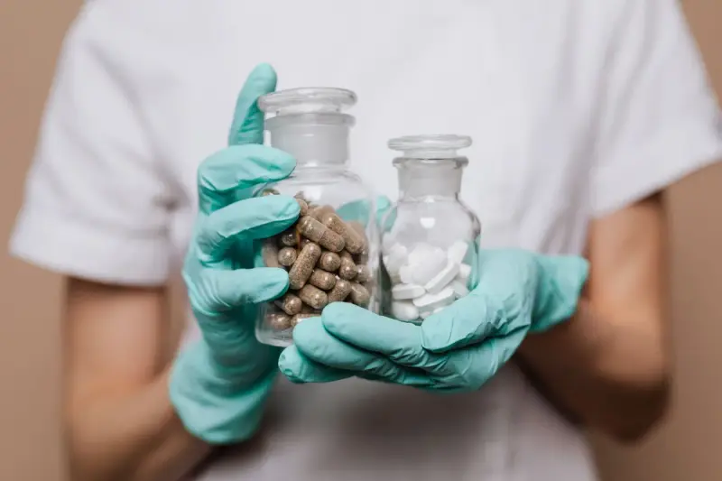 Gloved hands holding two glass jars of brown capsules and white tablets