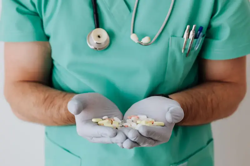 Clinician in green scrubs and gloves holding a handful of assorted pills