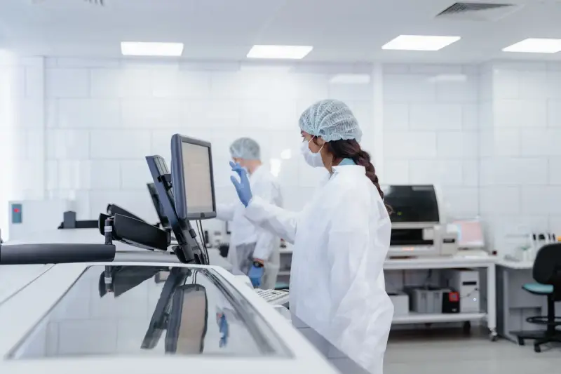 Technicians in caps and masks operating instruments in a bright white laboratory