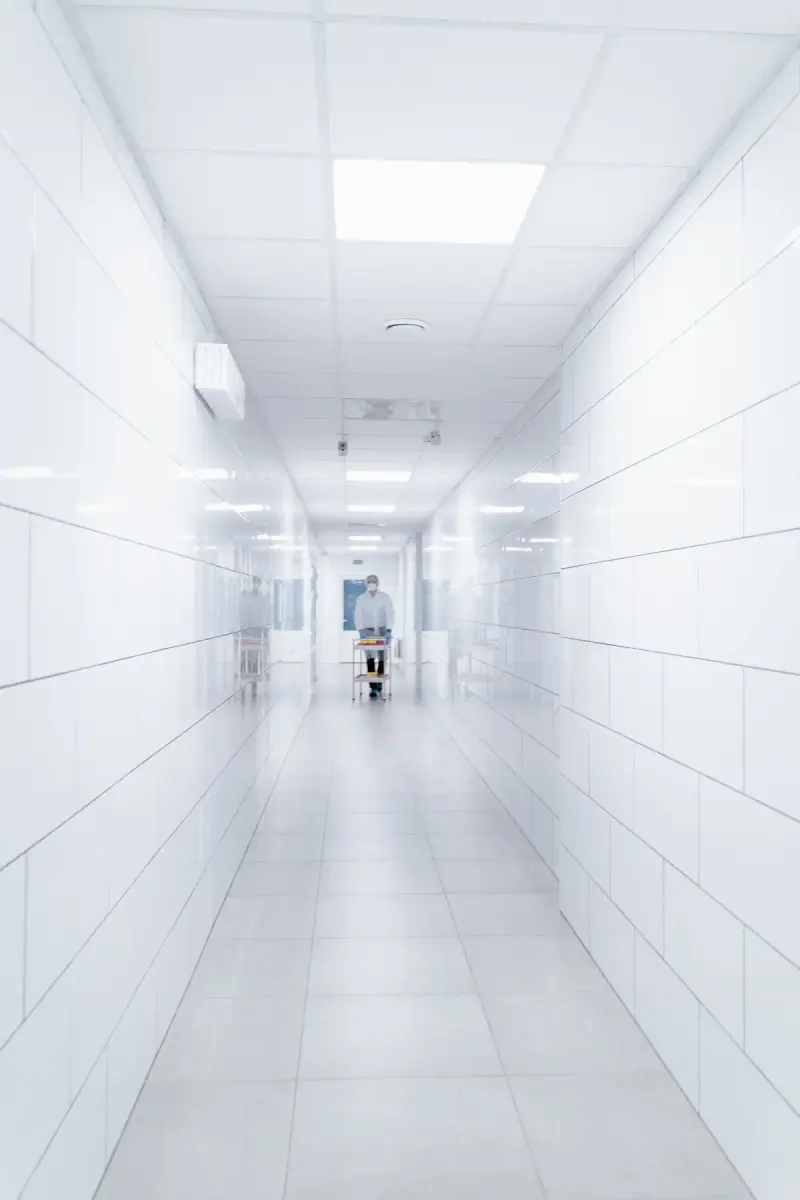 Bright white hospital corridor with a gowned worker pushing a cart in the distance