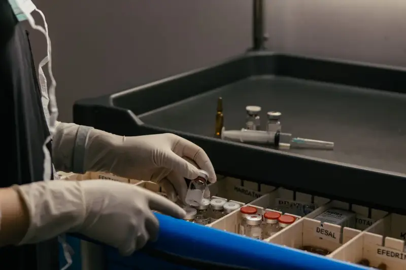Gloved hands sorting small vials in a hospital medication cart drawer