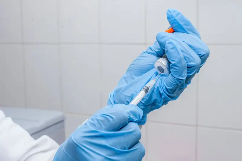 Hands in blue gloves drawing liquid from a vial into a syringe