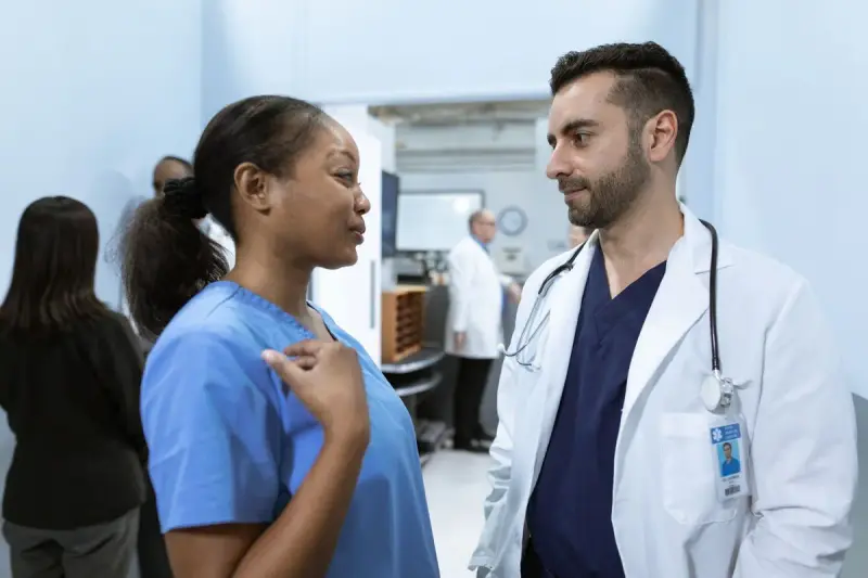Nurse in blue scrubs talking with a clinician in a white coat in a hospital unit