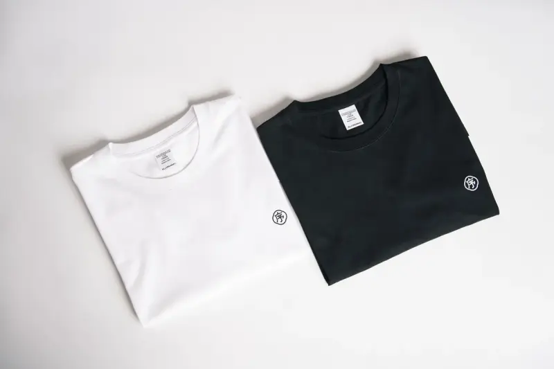 One white and one black folded t-shirt on a plain light background